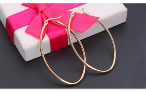Close-up of golden oval hoop earrings on white gift box with elegant magenta ribbon