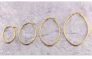 Detailed view of four sizes of gold-plated oval hoop earrings on marble background