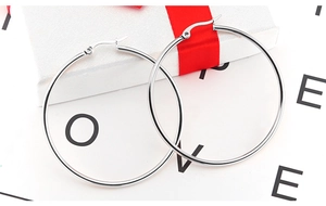 Detailed close-up of large polished silver hoop earrings placed on a festive gift box