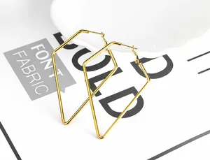 Detailaufnahme großer goldener geometrischer Rauten-Ohrringe auf weißem Porzellantablett