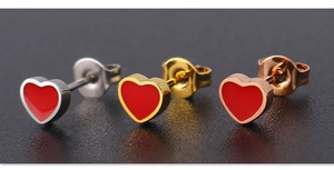 Macro shot of heart-shaped earrings in silver, gold, and rose gold with red enamel
