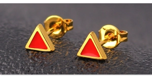 Macro view of gold triangle stud earrings with red enamel inlay and butterfly backs