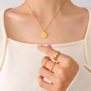 Collier à pendentif portrait abstrait et bagues dorées portés par un mannequin sur blanc