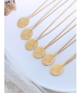 Dettaglio di pendenti ovali in oro con rose a rilievo e catene a croce su sfondo bianco