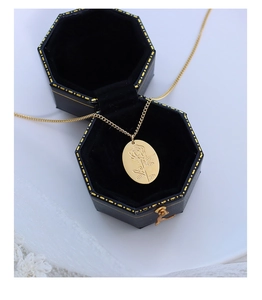 Collana con ciondolo ovale dorato e rosa incisa in una scatola regalo nera di velluto