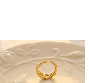 Detailed view of an adjustable gold-plated twisted ring on a decorative porcelain plate
