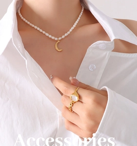 Close-up of pearl necklace with moon pendant and gold chain ring on a white shirt