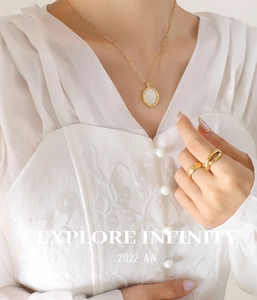 Détail du collier avec pendentif ovale en nacre blanche et bague dorée matelassée