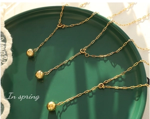 Detailed close-up of gold geometric sphere pendant necklaces on a green display plate
