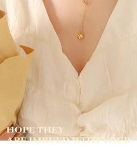 Close-up of a gold hammered sphere pendant necklace on a model wearing a pleated blouse