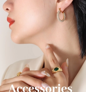 Close-up of elegant gold U-shaped earrings with rhinestones and a green gemstone ring