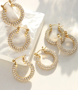 Detailed view of U-shaped gold earrings with paved white zircons on stone background