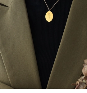 Close-up of golden oval flower pendant necklace styled with an olive blazer