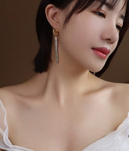 Dettaglio di eleganti orecchini pendenti dorati con zirconi taglio quadrato indossati da modella