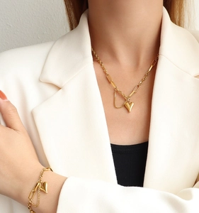 Détail de l'ensemble collier et bracelet cœur doré porté par un mannequin en blazer beige