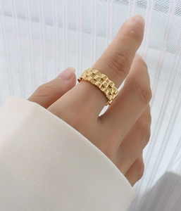 Detail eines goldfarbenen Rings im Uhrenarmband-Stil am Finger bei sanftem Licht