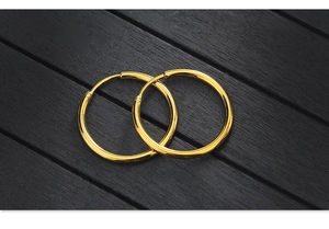 Polished gold hoop earrings in a minimalist circular design on a dark wood background