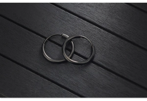Macro shot of minimalist matte black stainless steel hoop earrings on dark wooden background