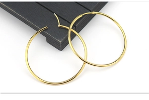Macro view of polished gold large hoop earrings with pin closure on a black wooden block