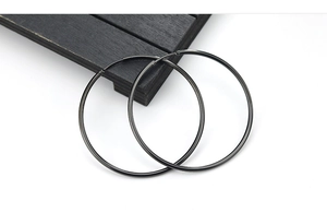 Close-up of minimalist matte black stainless steel hoop earrings on a wooden tray