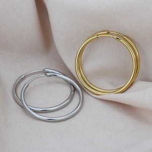 Minimalist gold and silver polished metal hoop earrings on soft pink fabric background