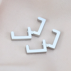 Detailed view of two pairs of silver U-shaped geometric clip earrings on silk fabric
