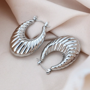 Détail macro de boucles d'oreilles créoles croissant en acier inoxydable argenté sur satin