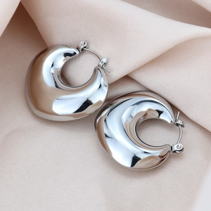 Détail de boucles d'oreilles créoles argentées épaisses sur un fond de satin champagne