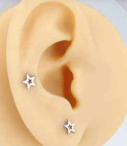 Macro shot of silver stainless steel star earrings on an ear model showing the hollow design