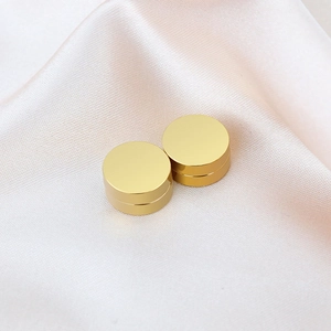 Makro-Detailansicht goldener Magnet-Ohrstecker auf edlem champagnerfarbenem Seidenstoff