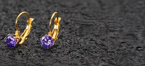 Dettaglio degli orecchini dorati a monachella con pietre tonde di zircone viola lucido