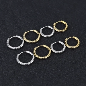 Detail van huggie-oorbellen in goud en zilver met gehamerde textuur en glans