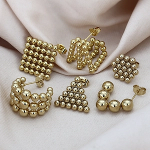 Set di orecchini a perno geometrici dorati con sei forme diverse su tessuto beige