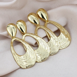 Exaggerated golden teardrop earrings with hollow irregular texture on pink silk