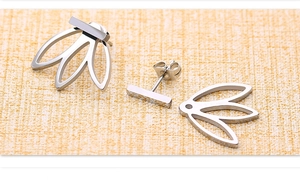 Détail de boucles d'oreilles trèfle argentées avec design à trois pétales sur tissu texturé