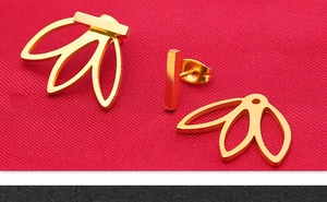 Vue macro des boucles d'oreilles dorées en éventail de feuilles sur tissu rouge texturé