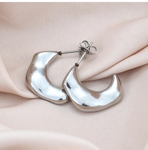 Close-up of irregular C-shaped titanium steel earrings with polished molten metal texture