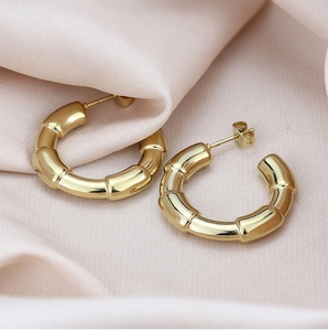 Detailed view of gold bamboo texture hoop earrings on elegant pink silk background