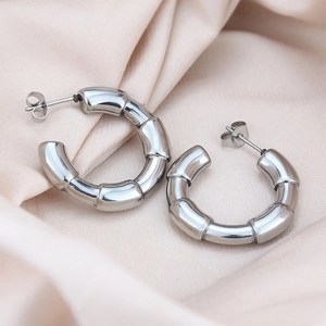 Detailed close-up of polished C-shaped bamboo texture stud earrings on soft silk fabric