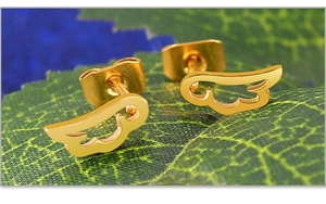 Macro shot of gold angel wing stud earrings with hollow design on green leaf