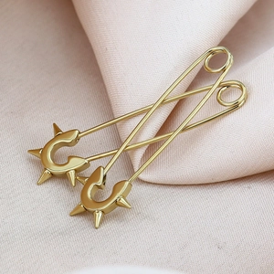 Detailaufnahme goldener Büroklammer-Ohrringe mit Punk-Stachel-Design auf rosa Satin-Stoff