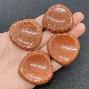 Detailed view of four heart-shaped goldstone worry stones held in a palm for size comparison