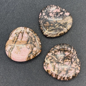 Detailed macro view of three heart-shaped polished rhodonite natural massage stones