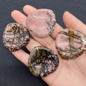 Close-up of heart-shaped pink rhodonite stones with black veins being held by a hand