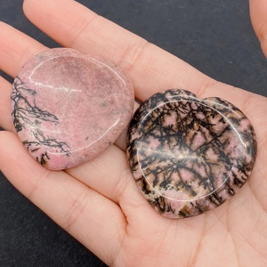 Close-up of heart-shaped polished rhodonite palm stones with natural black veins held in hand