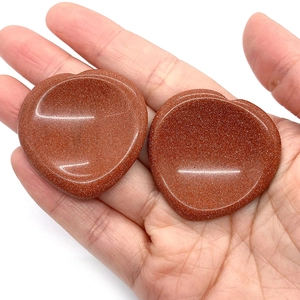 Natural heart-shaped goldstone thumb stones held in hand for size demonstration