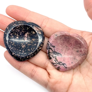 Polished heart-shaped natural worry stones in pink and black held in a hand for size
