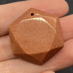 Macro detail of a hexagonal goldstone pendant showing golden sparkles and top drill hole