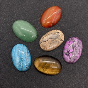 Close-up of polished oval gemstone cabochons including tiger eye and green aventurine