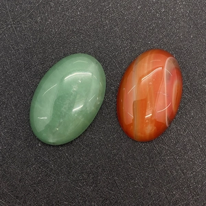 Polished oval green aventurine and red agate cabochons on a grey textured surface